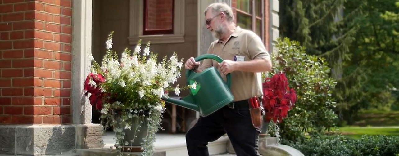Employee watering a large pot of flowers outside an academic building.