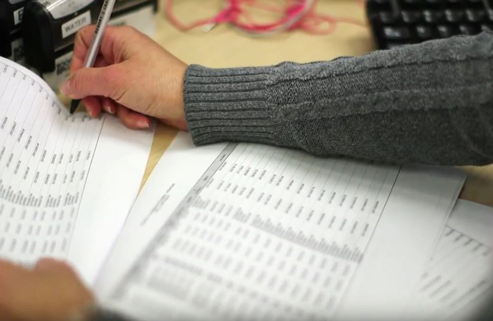 spreadsheet paperwork on desk with employee holding pen.