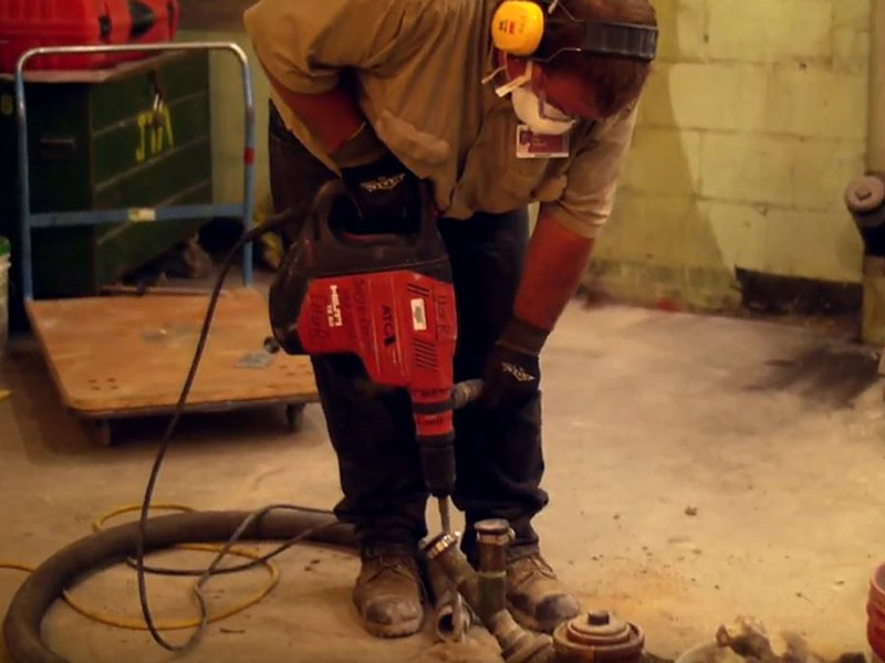 plumber using drill to access plumbing in concrete floor.